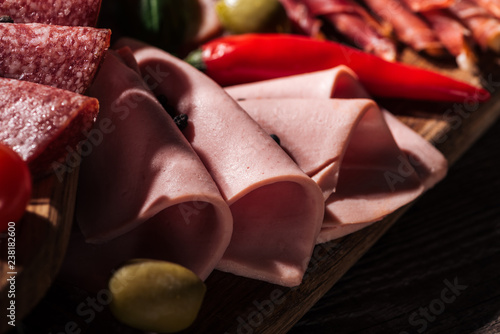close up view of wooden cutting board with tasty sliced ham and vegetables