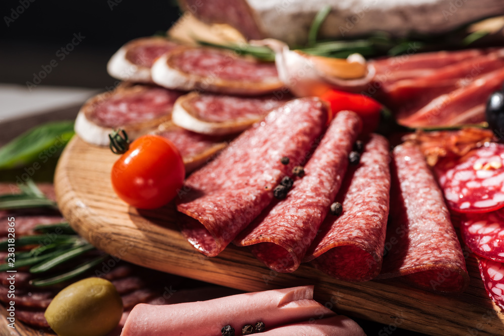 close up view of wooden cutting board with delicious sliced salami and vegetables