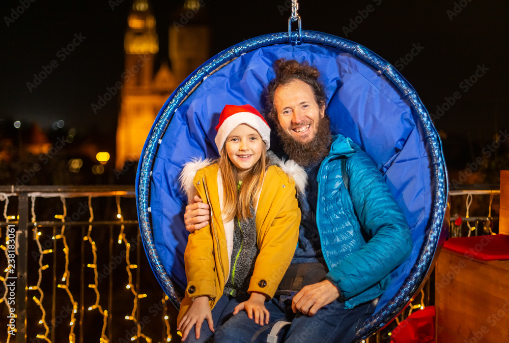 Father and daughter seated on hanging Christmas chairs.