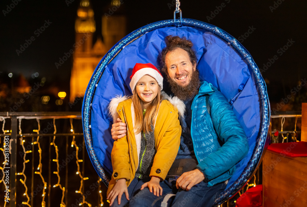 Obraz premium Father and daughter seated on hanging Christmas chairs.