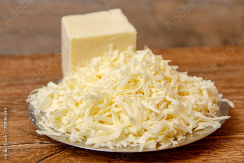Grated cheese on metal plate on wooden table ready for pizza