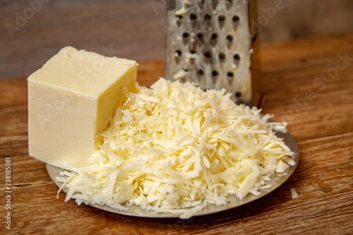 Grated cheese on metal plate on wooden table ready for pizza