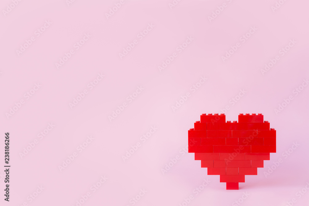 Red heart made of toy building bricks, viewed from the front, on pink background. Copy space.