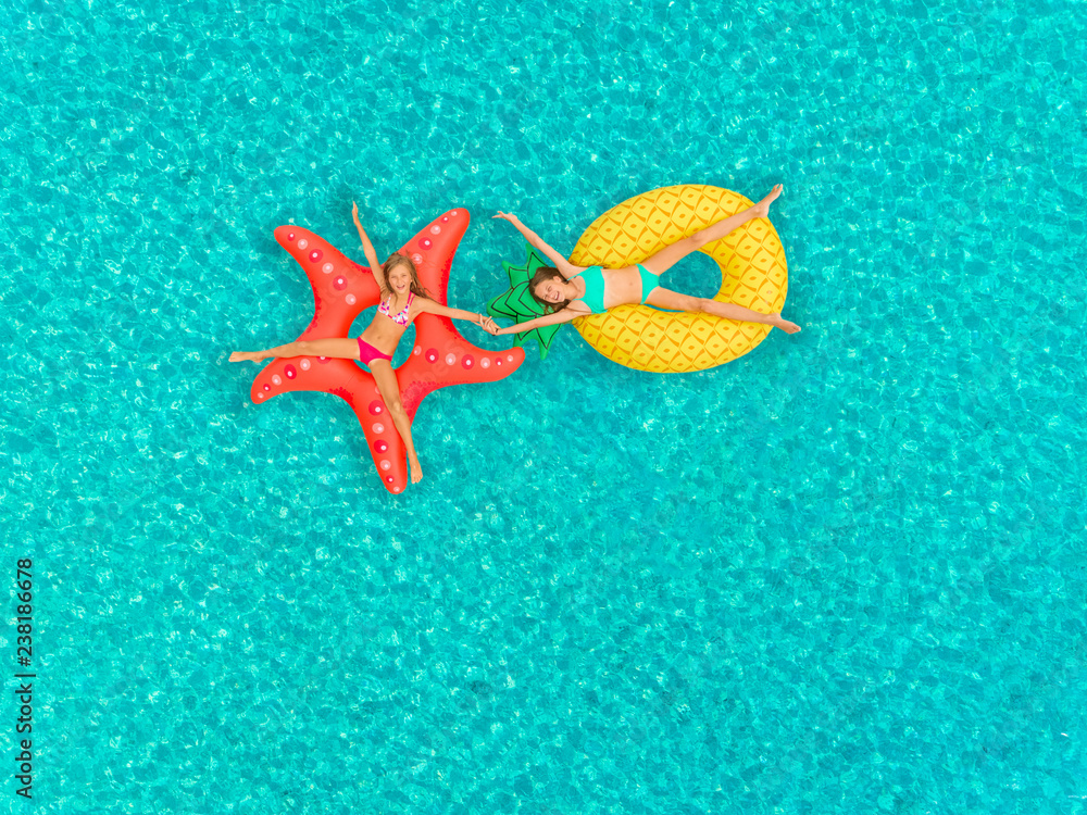 Aerial view of two girls floating on inflatable mattress holding hands. Aerial view of two girls floating on inflatable mattress holding hands.