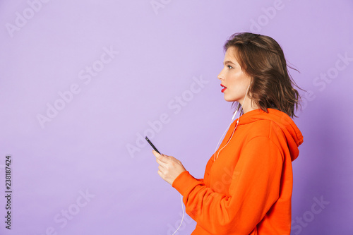 Beautiful young woman posing isolated over purple background wall listening music with earphones.