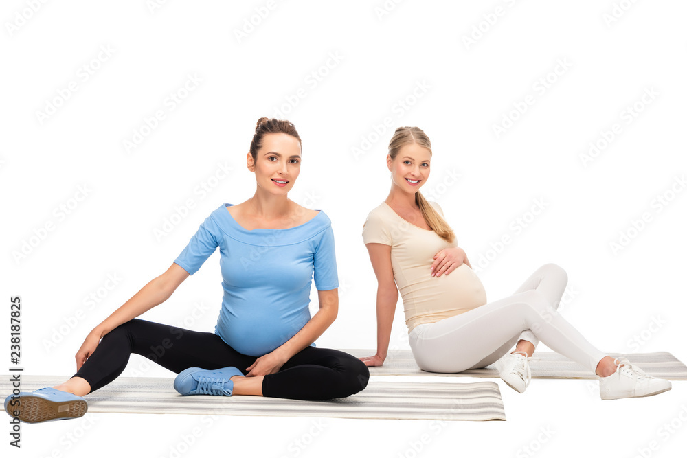 two pregnant women sitting on fitness mats isolated on white two pregnant women sitting on fitness mats isolated on white
