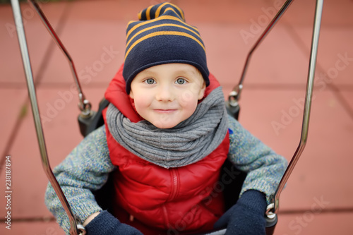 Cute little boy having fun on outdoor playground. Child on swing