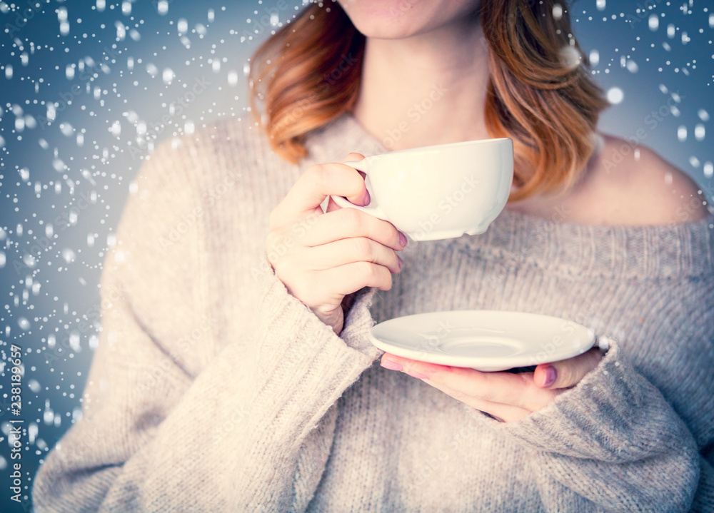 Portrait of young redhead woman in sweater with cup of coffee or tea on grey background. Image made with native lights Portrait of young redhead woman in sweater with cup of coffee or tea on grey background. Image made with native lights