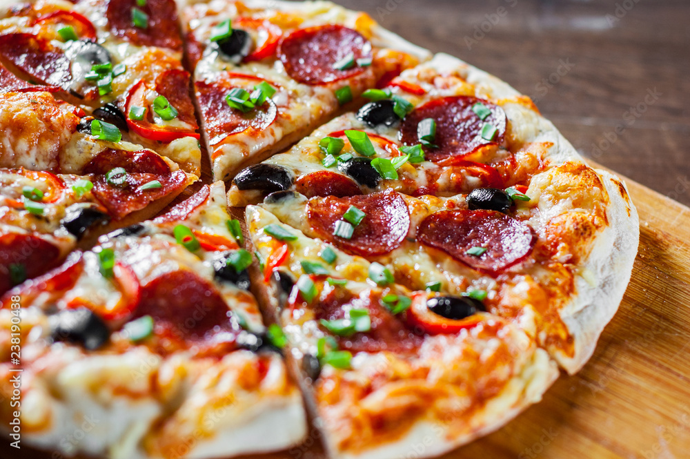 Pizza with Mozzarella cheese, pepperoni, tomato, pepper, olive, salami. Italian pizza on wooden table background Pizza with Mozzarella cheese, pepperoni, tomato, pepper, olive, salami. Italian pizza on wooden table background