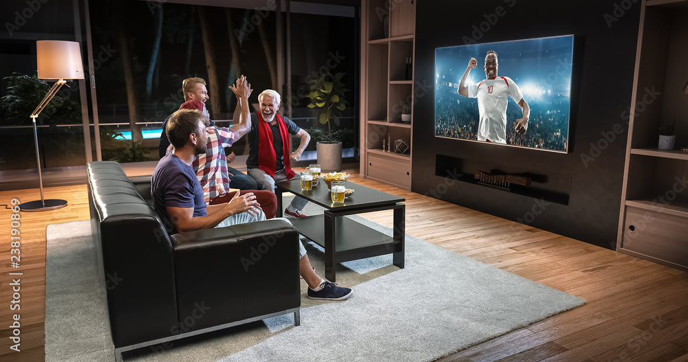 Group of fans are watching a soccer moment on the TV and celebrating a goal, sitting on the couch in the living room. Group of fans are watching a soccer moment on the TV and celebrating a goal, sitting on the couch in the living room.