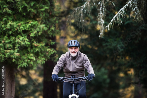 Active senior man with electrobike cycling outdoors on a road in nature.