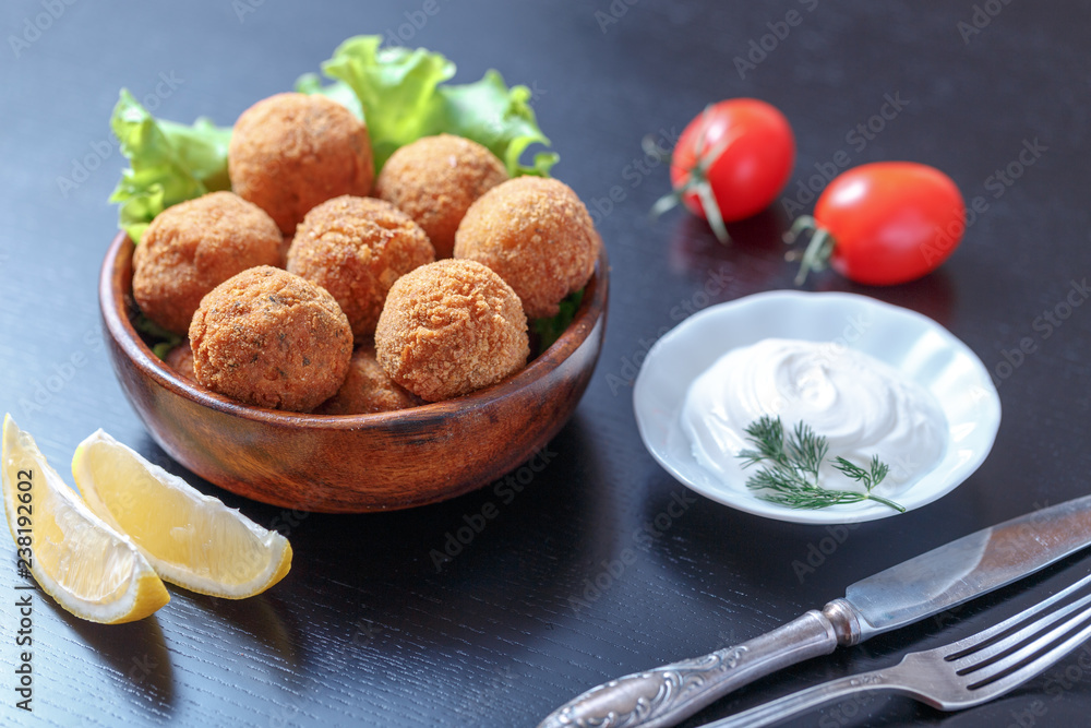 Falafel lies in a wooden plate. On the table lie tomatoes, cucumbers, lettuce, dill, lemon, sour cream. Falafel lies in a wooden plate. On the table lie tomatoes, cucumbers, lettuce, dill, lemon, sour cream.