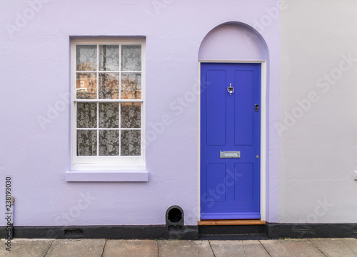 Typical english house facade with lavender color door and white window viewed from outdoors.