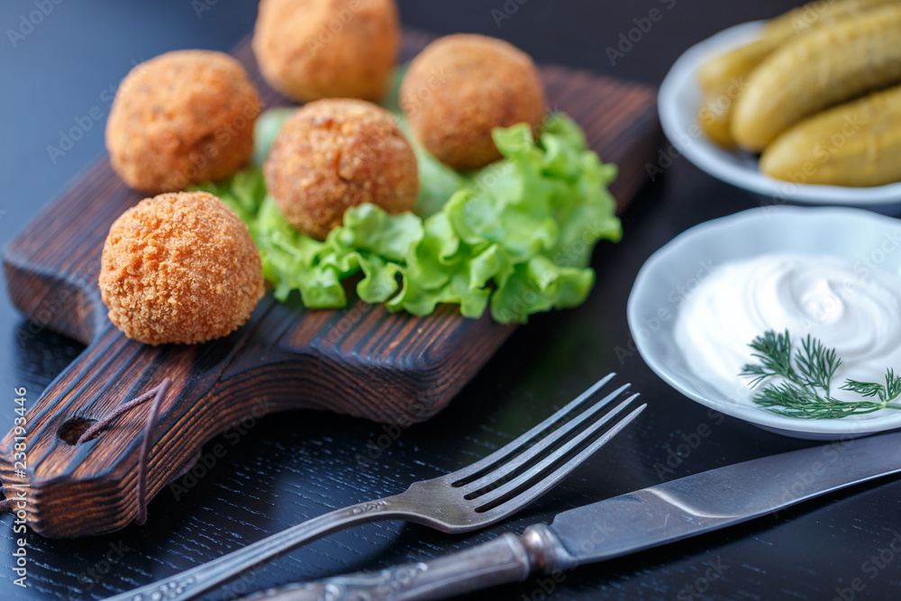 Falafel lies on a wooden cutting board. On the table lie tomatoes, cucumbers, lettuce, dill, lemon, sour cream. Falafel lies on a wooden cutting board. On the table lie tomatoes, cucumbers, lettuce, dill, lemon, sour cream.