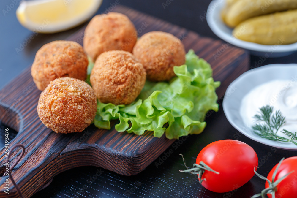 Falafel lies on a wooden cutting board. On the table lie tomatoes, cucumbers, lettuce, dill, lemon, sour cream. Falafel lies on a wooden cutting board. On the table lie tomatoes, cucumbers, lettuce, dill, lemon, sour cream.