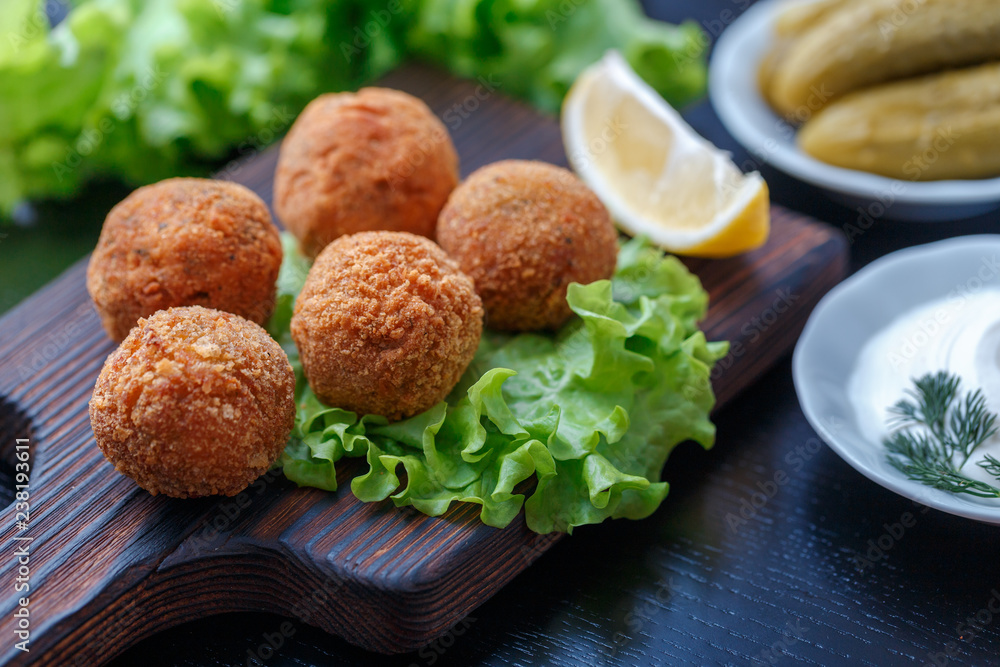 Falafel lies on a wooden cutting board. On the table lie tomatoes, cucumbers, lettuce, dill, lemon, sour cream. Falafel lies on a wooden cutting board. On the table lie tomatoes, cucumbers, lettuce, dill, lemon, sour cream.