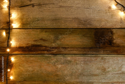 Flat lay of rustic and cracked wooden table with knots, with Christmas lights on the left. With copy space available.