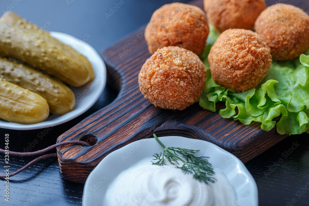 Falafel lies on a wooden cutting board. On the table lie tomatoes, cucumbers, lettuce, salad, dill, lemon, sour cream. Falafel lies on a wooden cutting board. On the table lie tomatoes, cucumbers, lettuce, salad, dill, lemon, sour cream.