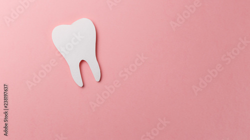 White tooth on pink background with copy space. Oral dental hygiene. Teeth whitening. Dental health concept. Oral care, teeth restoration. Dentist day concept. Flat lay. Top view. Pastel colors