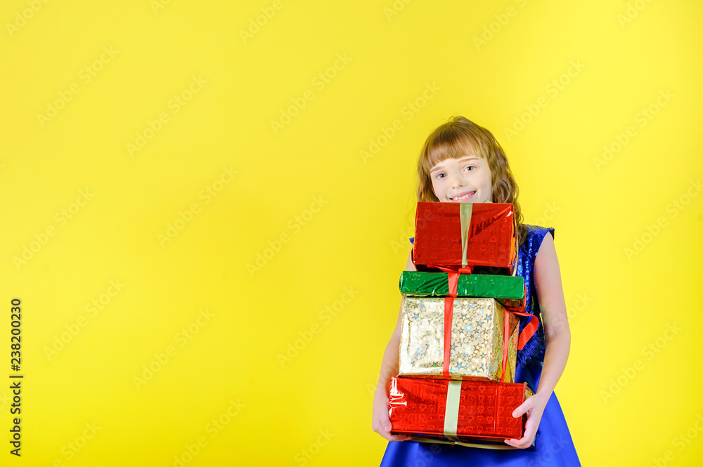 festive emotions, beautiful young girl in a festive blue dress holding a lot of gifts and smiling, in the studio on a yellow background festive emotions, beautiful young girl in a festive blue dress holding a lot of gifts and smiling, in the studio on a yellow background