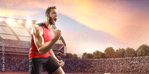 Happy male athlete. Man sprinter in sport clothes emotionally rejoices victory at the running track in professional stadium photo