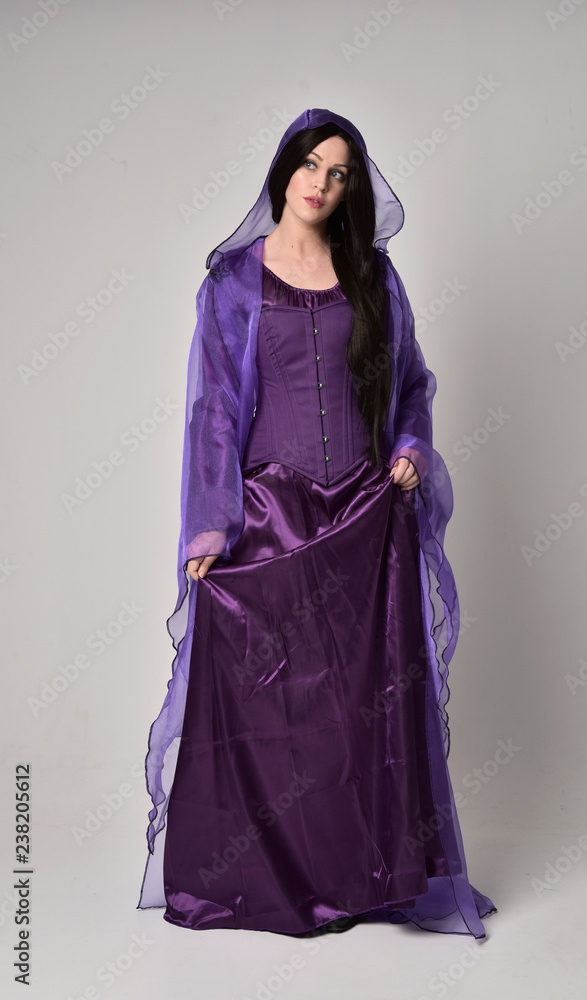 full length portrait of beautiful girl with long black hair, wearing purple fantasy medieval gown and cloak. standing pose on grey studio background. full length portrait of beautiful girl with long black hair, wearing purple fantasy medieval gown and cloak. standing pose on grey studio background.