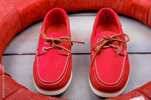 Red boat shoes on wooden background near lifebuoy. Top view. Close up