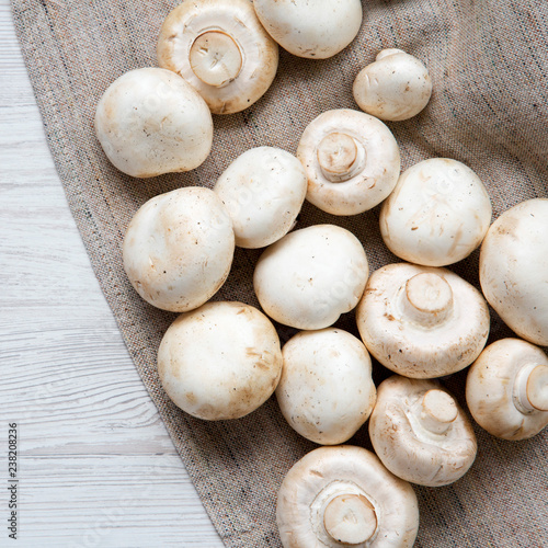 Fresh champignon mushrooms on cloth. White wooden background. Top view, from above, overhead.