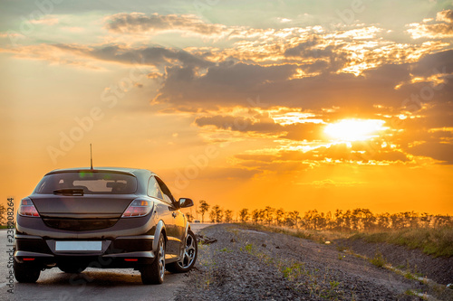 beautiful black modern car stands on asphalt road in summer illuminated by the rays of the sunset  © Ambartsumian