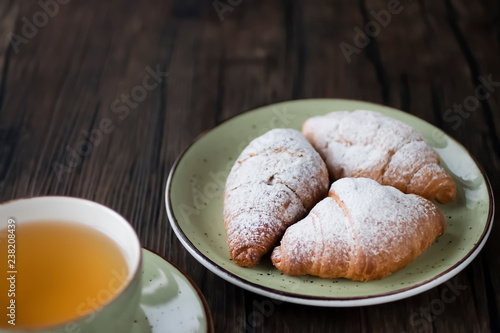 Freshly baked croissants cup with green tea on a brown wooden background.