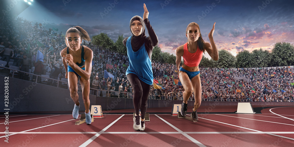 Female athletes sprinting. Women in sport clothes run at the running track  in professional stadium. Muslim athlete runs in sports hijab Stock Photo