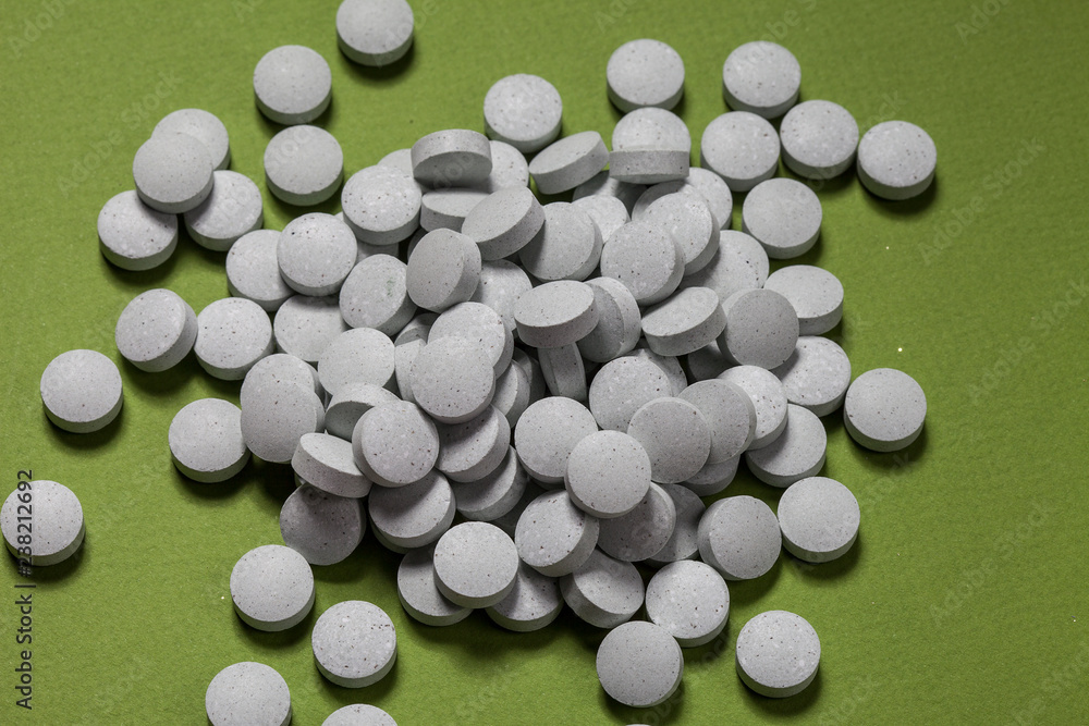 Round white pill in bulk on green background