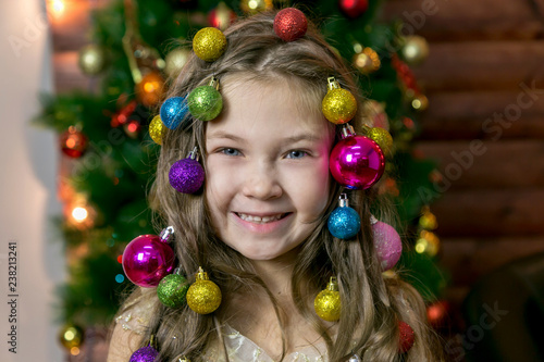 Girl with Christmas decorations in her hair. Little beautiful girl braided Christmas tree decorations in her hair.
