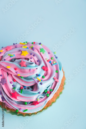 Closeup cupcake creamy multicolored top with colorful stars and sprinkles on blue background.