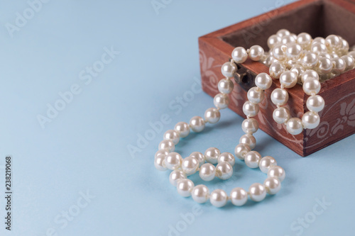 Pearl necklace in wooden box on light blue background. Copy space, close-up, soft focus