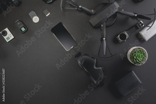 Work space photographer with laptop, digital camera, memory card, action camera, drone, remote controller, phone, VR glasses and camera accessory. Top view on black table background. 
