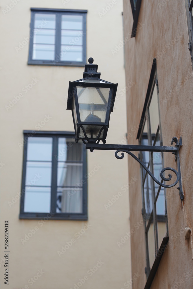 Stockholm old town. Old forged lantern on a light brown wall surrounded by houses with windows.