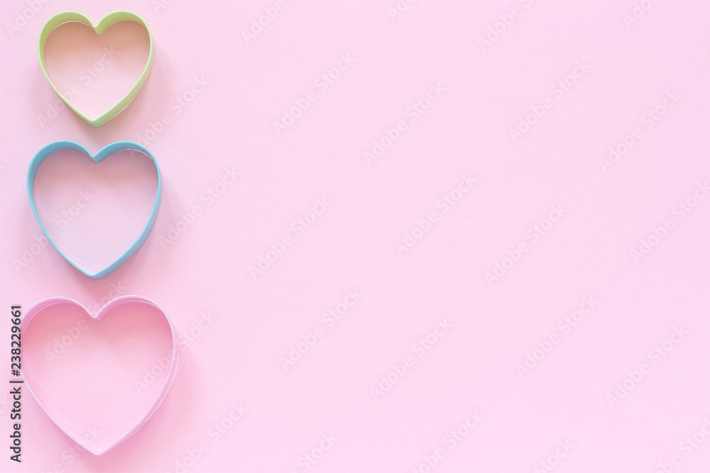 Colorful cutters cookies in heart shape on pastel pink background. Concept Valentine's card. Top view Copy space for text.