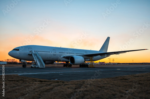 White wide body passenger airplane with boarding steps at the airport apron in evening twilight