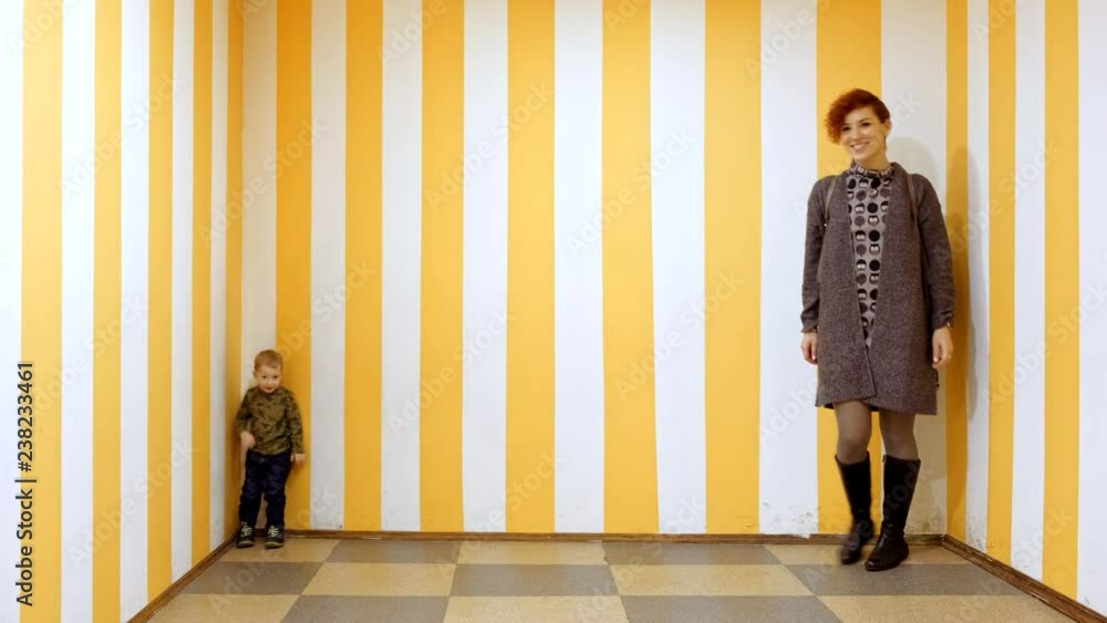 Happy kid boy and mother having fun in entertainment game center on family holidays. Illusion and surreal optical effect of small and big person while changing places. Little child and woman playing.