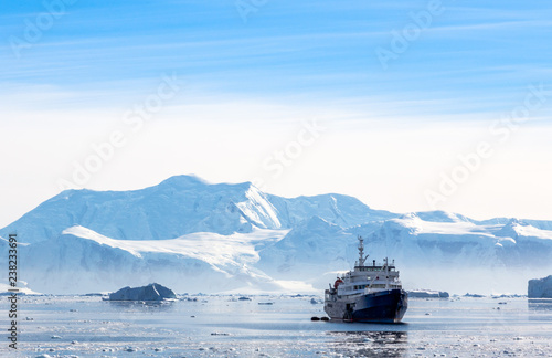 Touristic antarctic cruise liner drifting in the lagoon among the icebergs with glacier in background, Neco bay, Antarctica photo