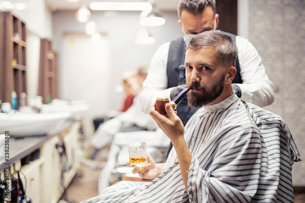 Hipster man client visiting haidresser and hairstylist in barber shop, smoking a pipe. Hipster man client visiting haidresser and hairstylist in barber shop, smoking a pipe.