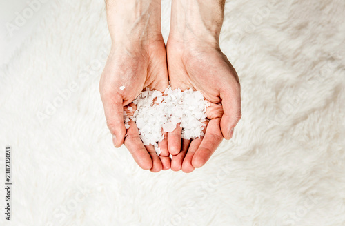 Close up view of man hands holding Magnesium Chloride vitamin salt flakes in palms hands, isolated on white soft fur background. Ingredient for making feet bath with Magnesium salt  Lot of copy space. photo