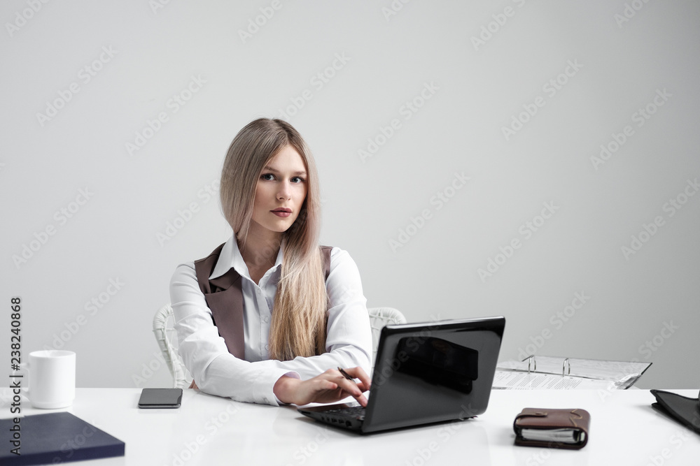 Blonde girl in a business suit works on a computer in a white bright office. Blonde girl in a business suit works on a computer in a white bright office.