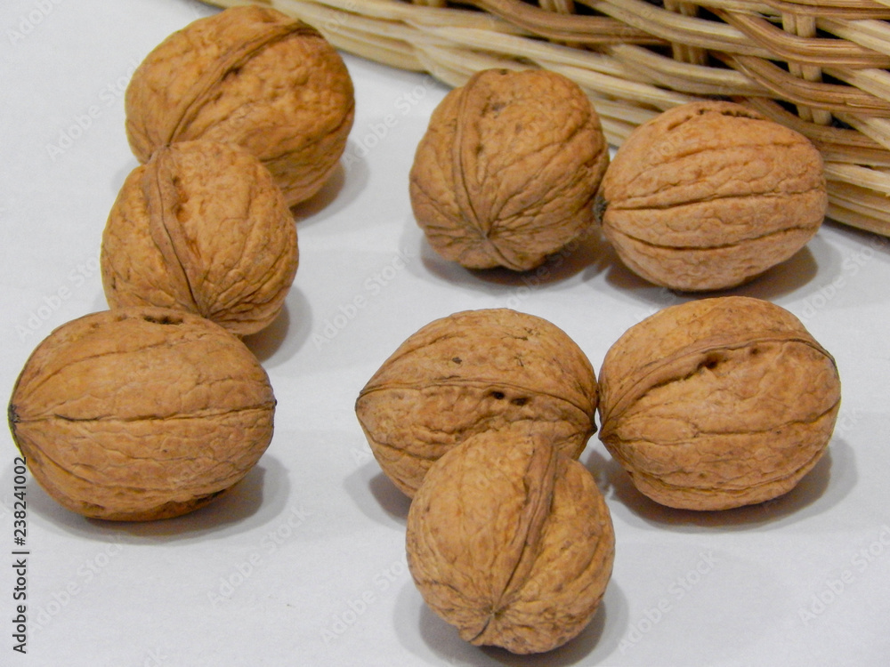 Walnuts in front of a basket on a white background
