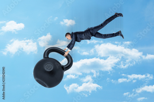 A young businessman in mid air gripping hold of a disproportionately big kettlebell with number 32 on it. photo