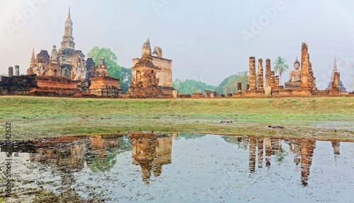 View of a Buddha statue seated among decadent columns of a ruined shrine in Wat Mahathat, an ancient Buddhist Temple and a beautiful UNESCO heritage site in Sukhothai Historical Park in Thailand, Asia