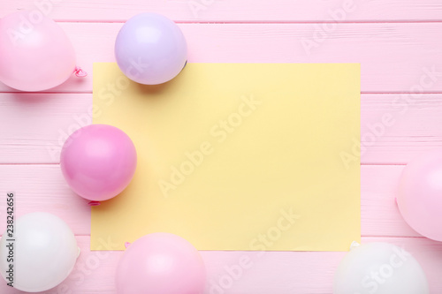 Colorful balloons with sheet of blank paper on pink wooden table