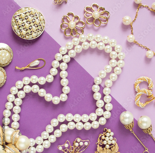 Woman's Jewelry. Vintage jewelry background. Beautiful gold tone and pearls brooches, braceletes, necklaces and earrings on purple background. Flat lay, top view.