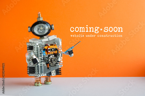 Web site under construction Coming Soon page. Toy robot with screwdriver and light bulb. Orange wall gray floor background.